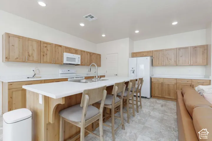 Kitchen featuring light wood cabinetry, white countertops, a large center island, and white appliances