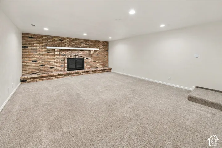 Spacious room featuring a brick fireplace with a white mantel, light-toned carpeting, and recessed lighting