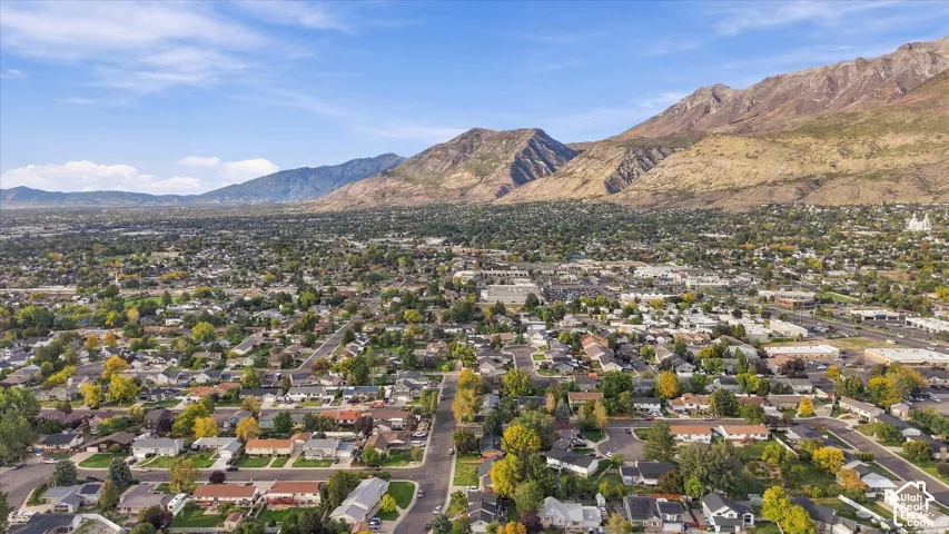Aerial perspective of a developed residential area with established trees, framed by a mountainous backdrop under a clear sky