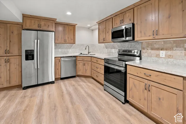 Kitchen featuring wood-finish cabinetry, stainless steel appliances, light-toned countertops, and a tile backsplash