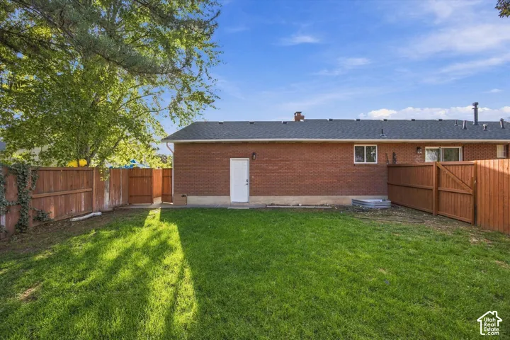 Expansive green lawn, wood fence, brick exterior, white service door, and a sliding glass door