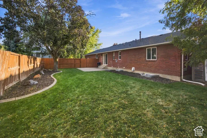 Expansive backyard featuring a manicured lawn, wood fencing, mature tree, concrete patio, and a brick exterior