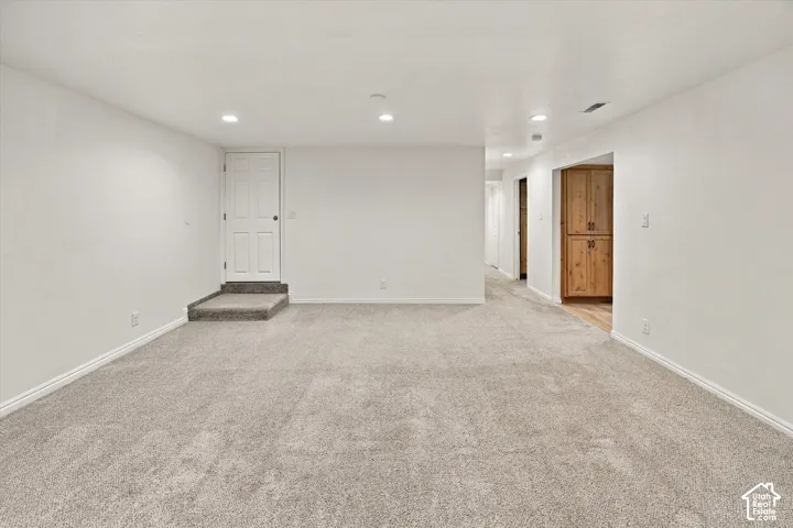 Expansive room featuring light gray carpeting, recessed lighting, white walls, and a built-in wood-finish cabinet