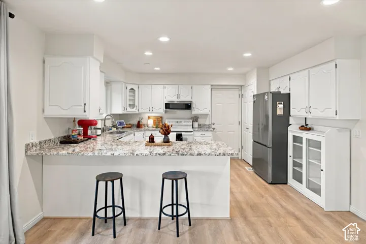 Kitchen featuring white cabinetry, light-toned wood-finish flooring, a breakfast bar, recessed lighting, and integrated appliances