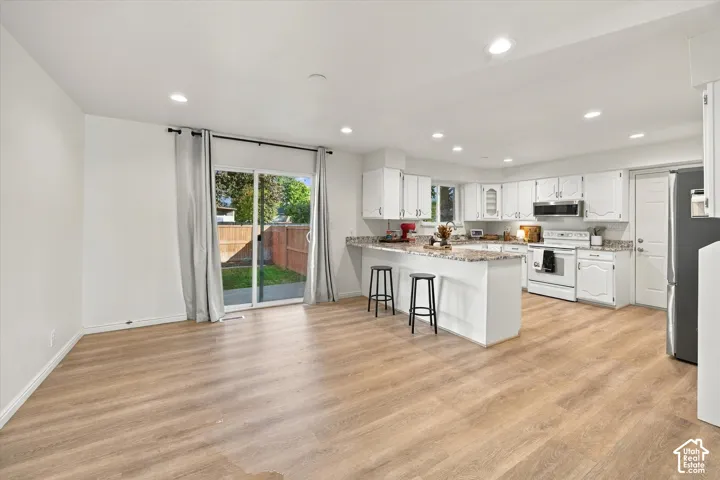 Open-concept living space with wood-finish flooring, recessed lighting, and a kitchen featuring white cabinetry and light-toned countertops