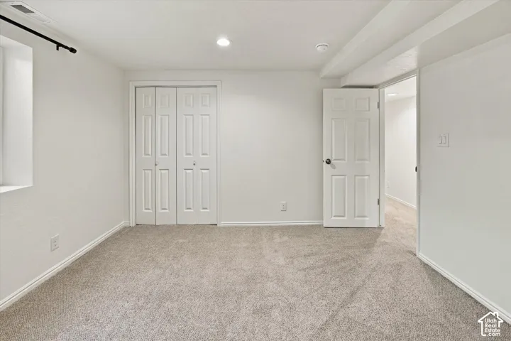 Neutral-toned carpeting, white walls, recessed ceiling lighting, and a bi-fold closet