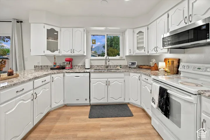 White cabinetry, wood-finish flooring, undermount sink, built-in microwave, and a window above the sink