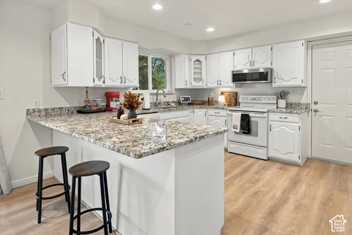 Kitchen featuring white cabinetry, granite-finish countertops, wood-finish flooring, a stainless steel microwave, and white appliances