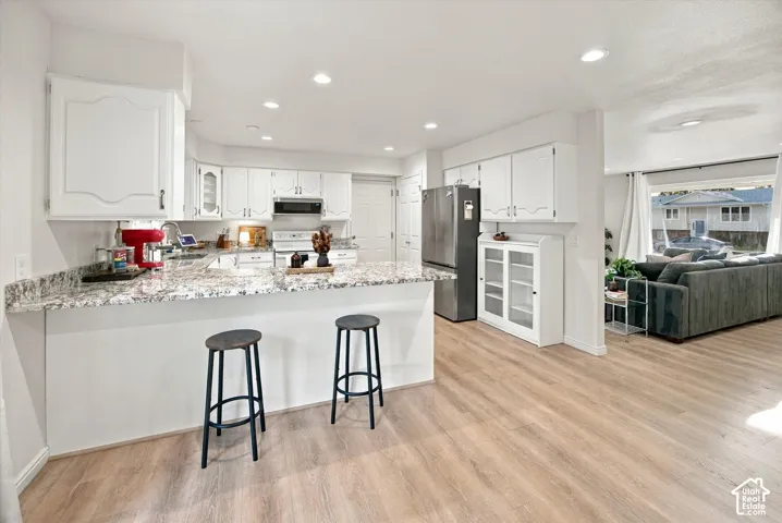 Kitchen featuring light-toned wood-finish flooring, white cabinetry, speckled countertops, and recessed lighting