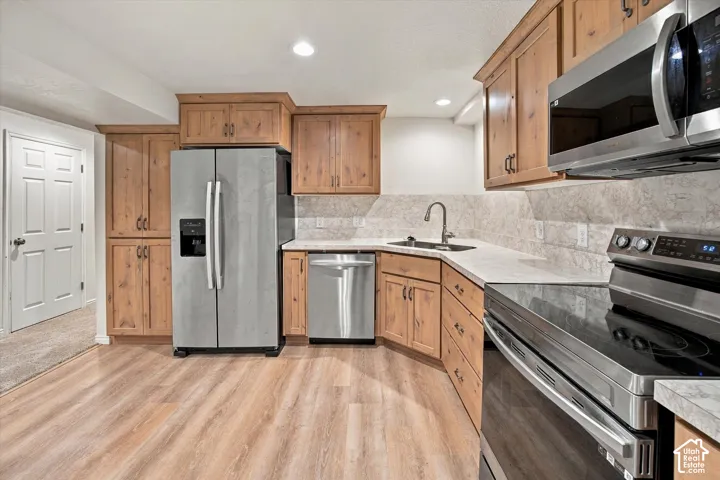 Wood-finish flooring, light wood cabinetry, stainless steel appliances, stone-look countertops, and a tiled backsplash