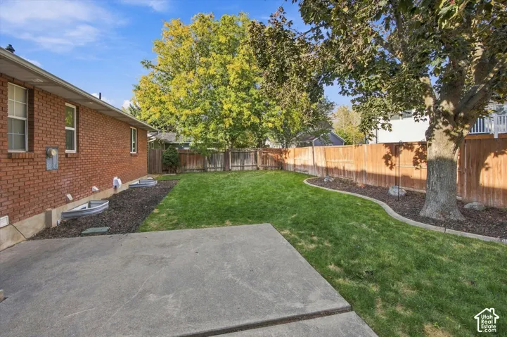 Expansive backyard featuring a manicured lawn, concrete patio, mature trees, and privacy fencing