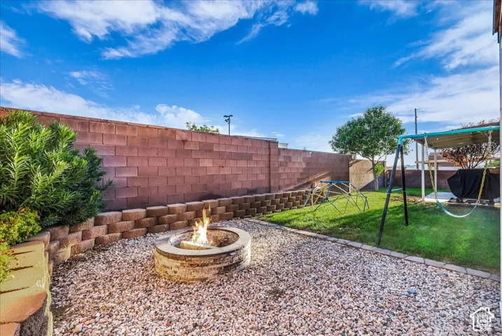 Outdoor area featuring a built-in fire pit with gravel surround, a retaining wall, and a grassy expanse