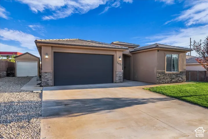 Stucco exterior with stone accents, a dark garage door, and an attached storage shed