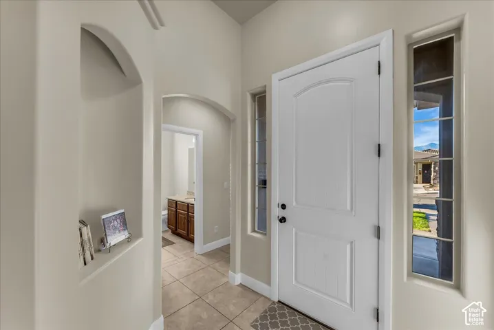 Archway entry with recessed niche, tiled flooring, white paneled door, and sidelight windows