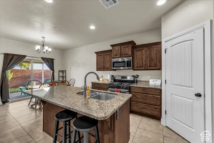 Kitchen island with integrated sink, stainless steel appliances, wood cabinetry, tile flooring, and a sliding glass door to the exterior