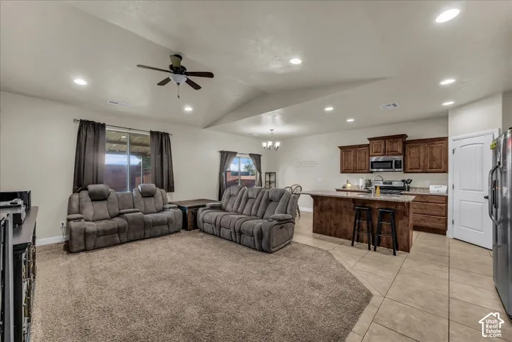 Vaulted ceiling with a ceiling fan, recessed lighting, wood-finish cabinetry, stainless steel appliances, and a kitchen island with seating