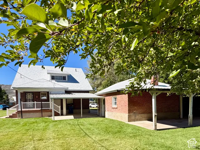 Expansive grassy yard with covered parking, a separate brick structure, and a brick-clad residence featuring a dormer window