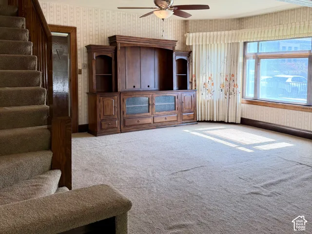 Broadloom carpeting, wood-finish staircase, built-in wooden media console, ceiling fan with integrated lighting, and multiple windows