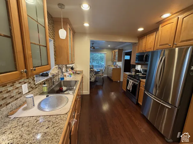 Kitchen featuring wood-finish cabinetry, stainless steel appliances, granite countertops, and a mosaic tile backsplash