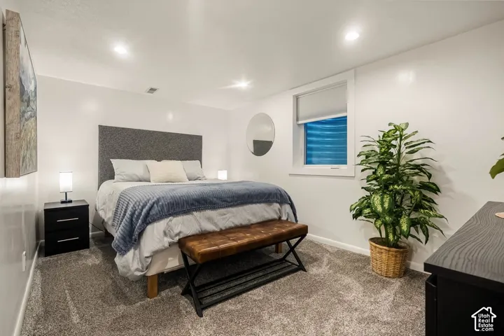 Carpeted room featuring a window with roller shade, recessed lighting, and white walls