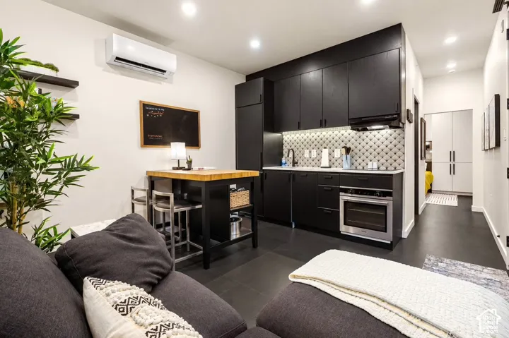 Modern kitchen featuring black cabinetry, light-toned countertops, a geometric pattern backsplash, and an integrated oven