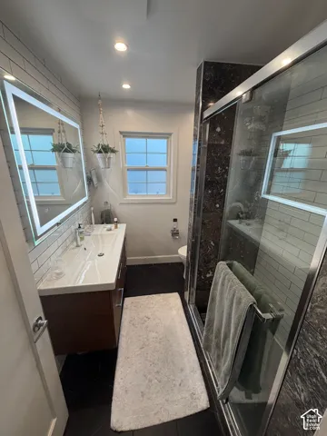 Floating vanity with integrated sink, backlit mirror, subway tile wall, recessed lighting, and a glass-enclosed shower with dark stone-finish walls