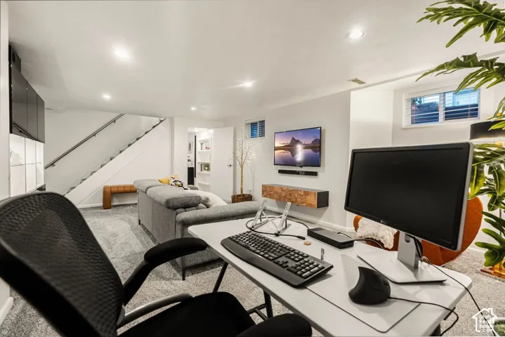 Recessed lighting, wall-mounted television, floating wood-finish media console, built-in open shelving, and a modern staircase with a metal handrail