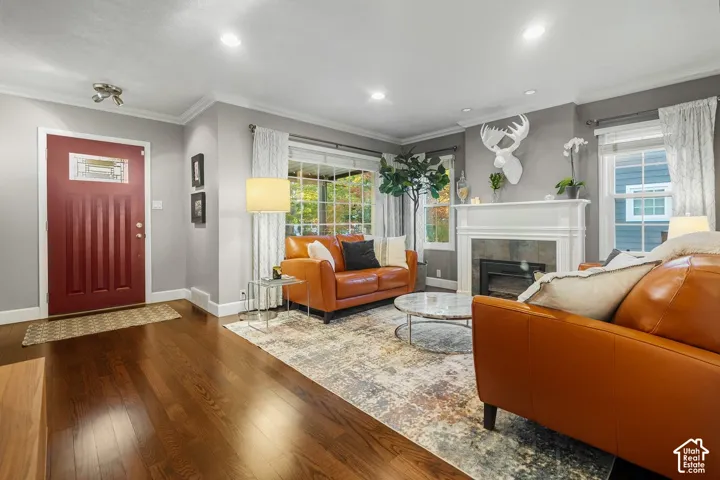 Hardwood flooring, recessed lighting, crown molding, white fireplace surround with dark stone hearth, and a red entry door with decorative glass inserts