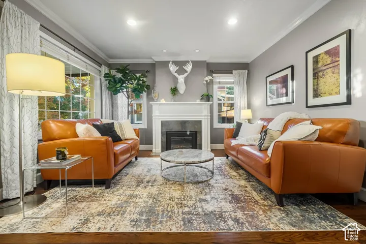 Hardwood flooring, crown molding, a fireplace with a white mantel, and recessed lighting