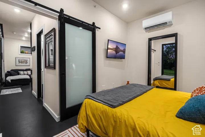 Sleek black flooring throughout, featuring a modern barn door with frosted glass panel, wall-mounted television, and a ductless mini-split system