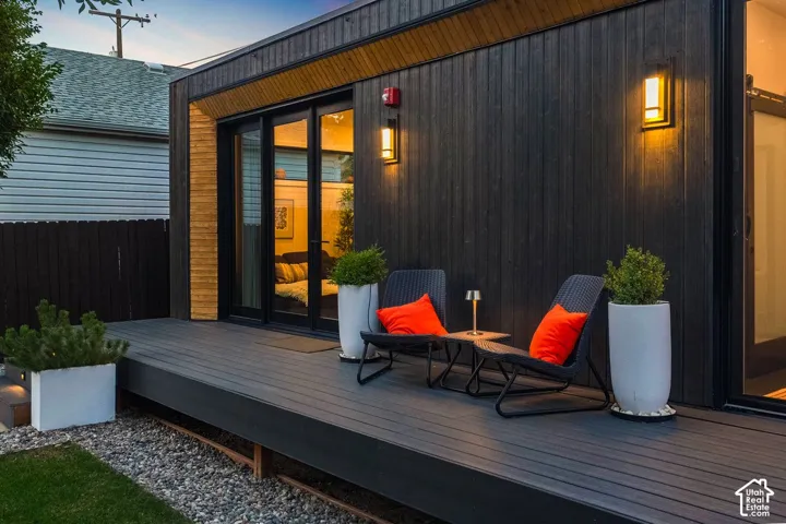 Dark wood-paneled exterior with two wall-mounted exterior lights, a multi-panel sliding glass door, and an expansive composite deck
