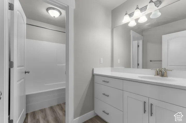 White vanity with brushed nickel hardware, expansive vanity mirror, integrated sink, and a combination shower/tub