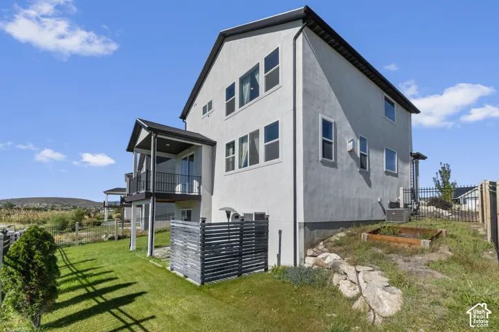 Multi-story exterior with stucco finish, multiple windows, covered balcony with metal railing, and a sloped grassy yard