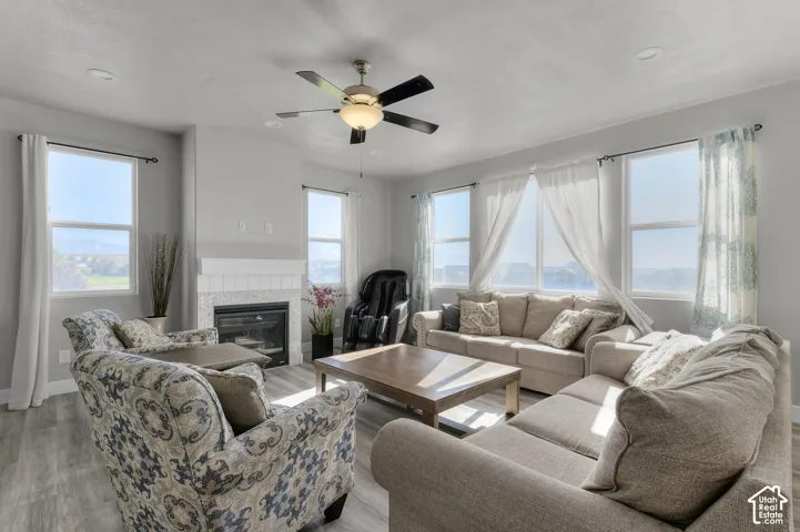 Spacious living area featuring a central fireplace with tile surround, multiple windows, wood-finish flooring, recessed lighting, and a ceiling fan
