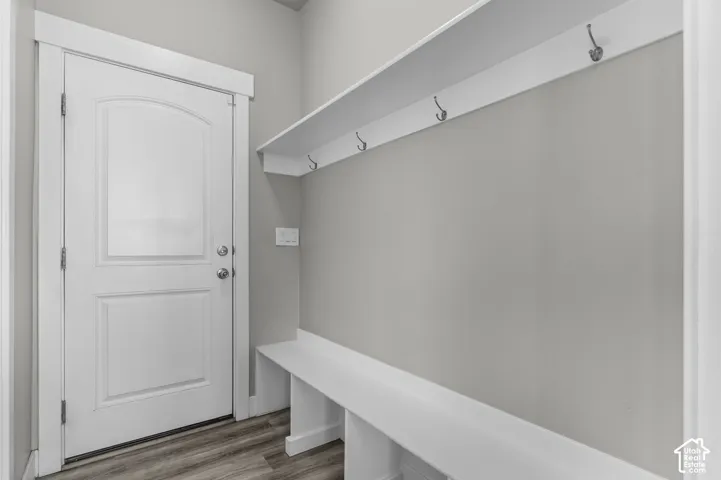 Built-in storage bench with overhead shelving and coat hooks, arched panel door, and wood-finish flooring