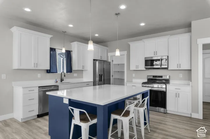 Modern kitchen featuring white shaker-style cabinetry, a contrasting blue island with seating, stainless steel appliances, and wood-finish flooring