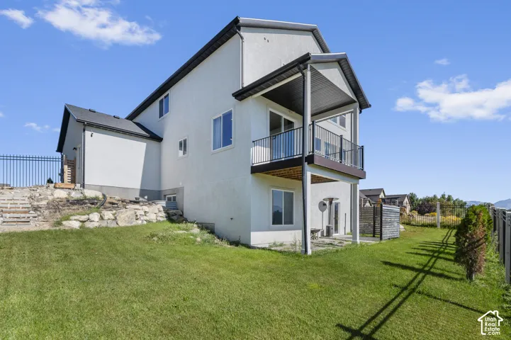 Stucco exterior, upper-level balcony with black railing, lower-level patio, sloped backyard, and metal perimeter fencing