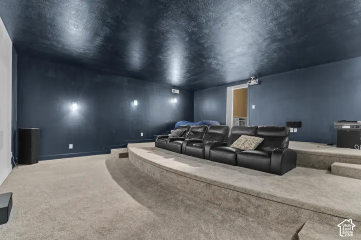 Tiered media room featuring carpeted flooring, wall-mounted sconces, and a projector