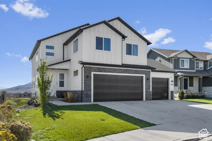 Contemporary two-story exterior with white siding and dark trim, featuring a two-car garage with dark doors, a concrete driveway, and a manicured lawn