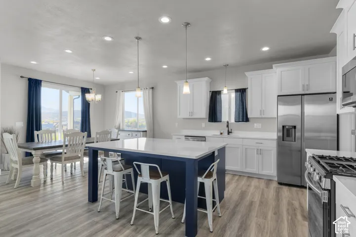 Spacious kitchen featuring a large central island with seating, stainless steel appliances, abundant white cabinetry, and light wood-finish flooring