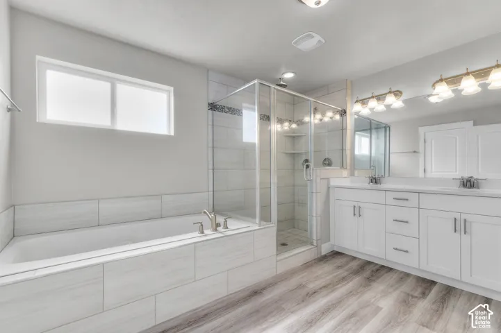 Spa-inspired primary bathroom featuring a freestanding soaking tub with subway tile surround, a frameless glass-enclosed walk-in shower with multiple showerheads, dual-sink vanity with white cabinetry and chrome hardware, wood-finish flooring, and integra