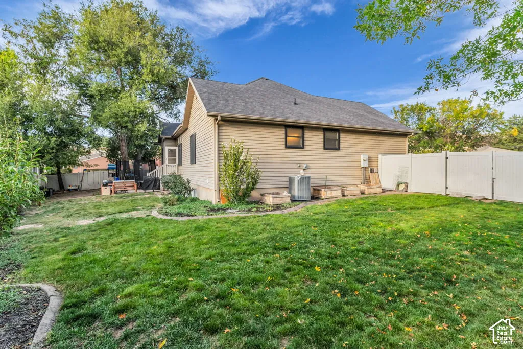 Expansive backyard featuring a manicured lawn, established trees, tan siding, and a white privacy fence