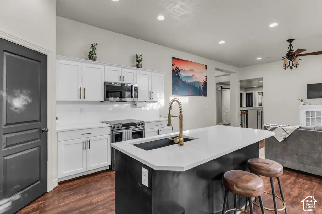 Kitchen featuring a central island with a gold-finish faucet, white cabinetry, dark wood-finish flooring, and recessed lighting