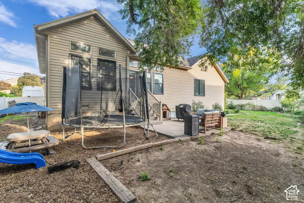 Rear exterior featuring horizontal siding, a concrete patio, and a tiered backyard with mature trees