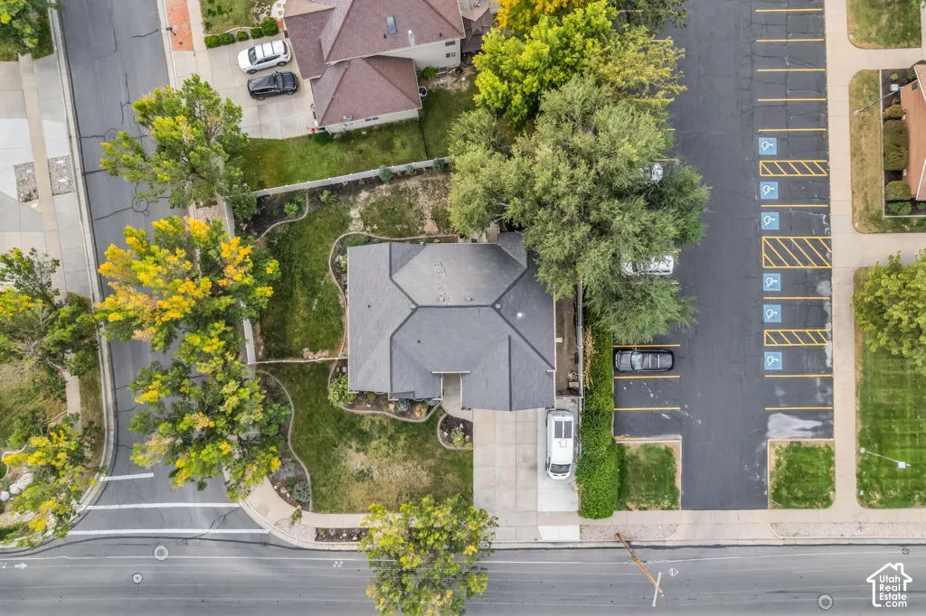 Gable roofline with dark shingles, concrete driveway, landscaped yard with established trees, paved street, and nearby asphalt parking area