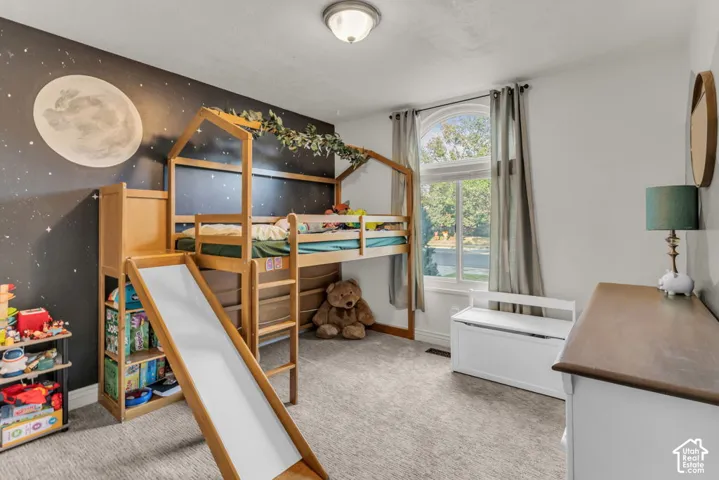 Arched window with light-filtering curtains, overhead flush mount light fixture, plush carpet flooring, and a decorative accent wall