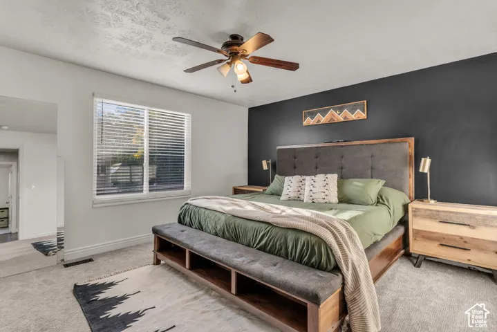 Spacious bedroom featuring light-colored carpeting, a window with blinds, and a ceiling fan