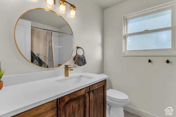 Vanity with a white countertop and wood-finish cabinetry, gold-tone fixtures, and an oval mirror