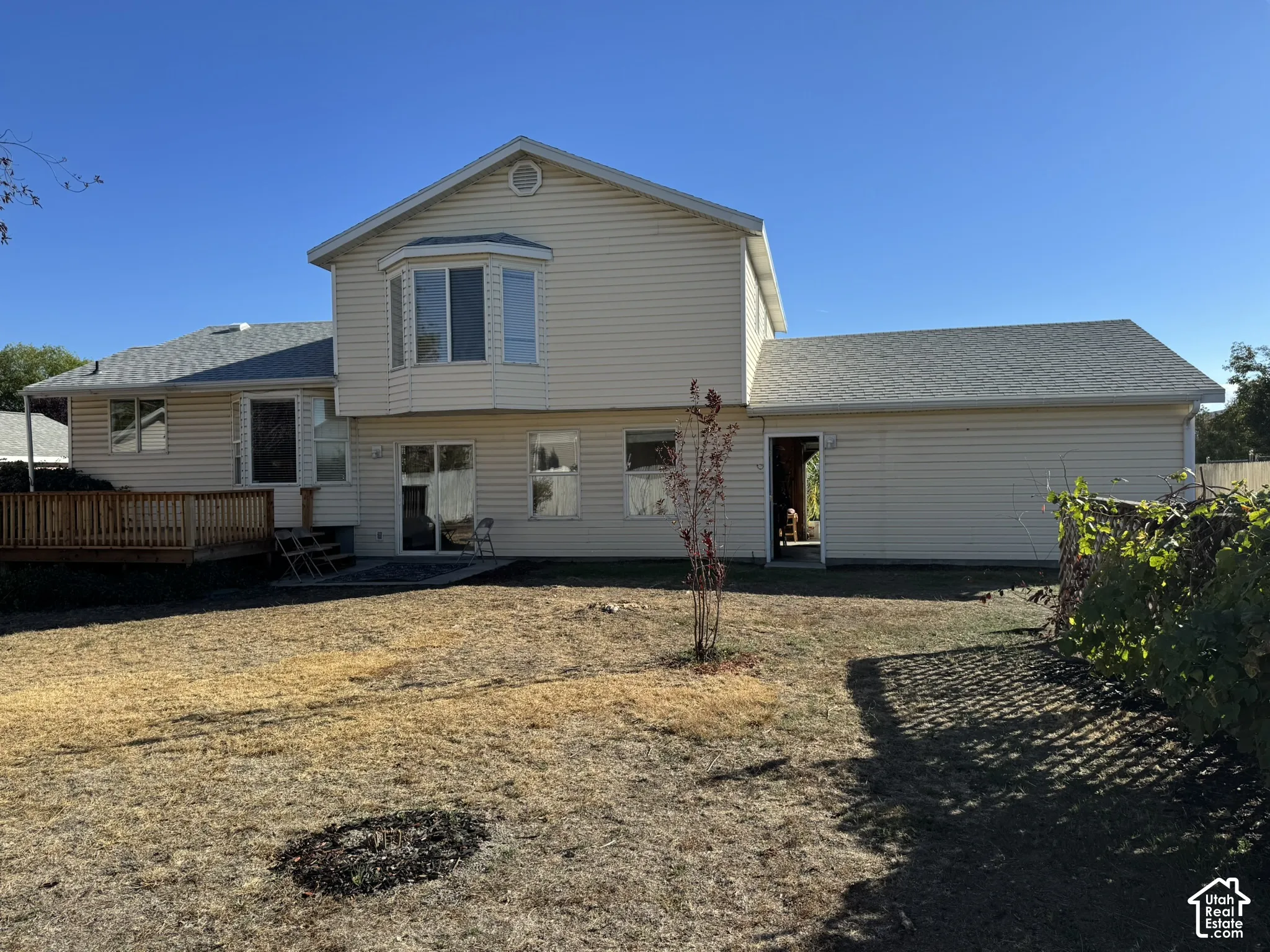 Rear exterior with light-colored siding, a wood deck, a bay window, and a sliding glass door