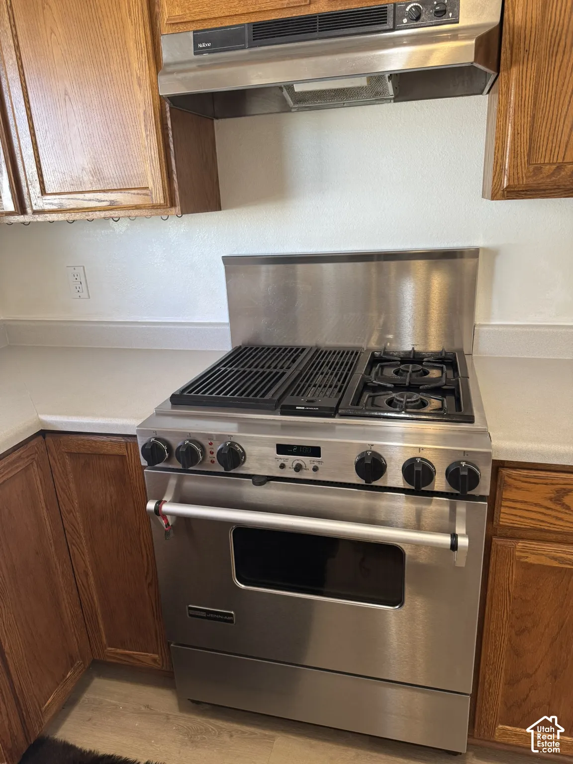 Stainless steel range with integrated griddle, coordinating stainless steel backsplash, and wood-finish cabinetry